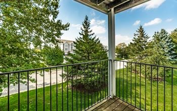 A balcony with a black railing and a view of a tree and a buildin